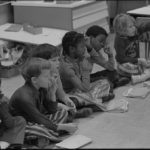 First grade class of African American and white school children seated on the floor
